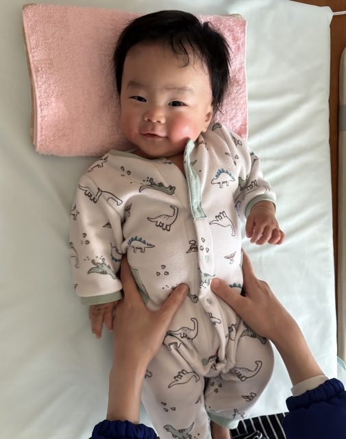 笑顔であおむけに寝転ぶ赤ちゃん。お腹のマッサージ中で、安心した表情を見せています(米子市 子育て長田こどもクリニック)